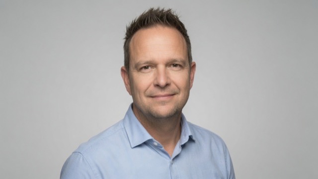 Portret van Theo van der Sluijs in een lichtblauw overhemd voor een lichtgrijze achtergrond