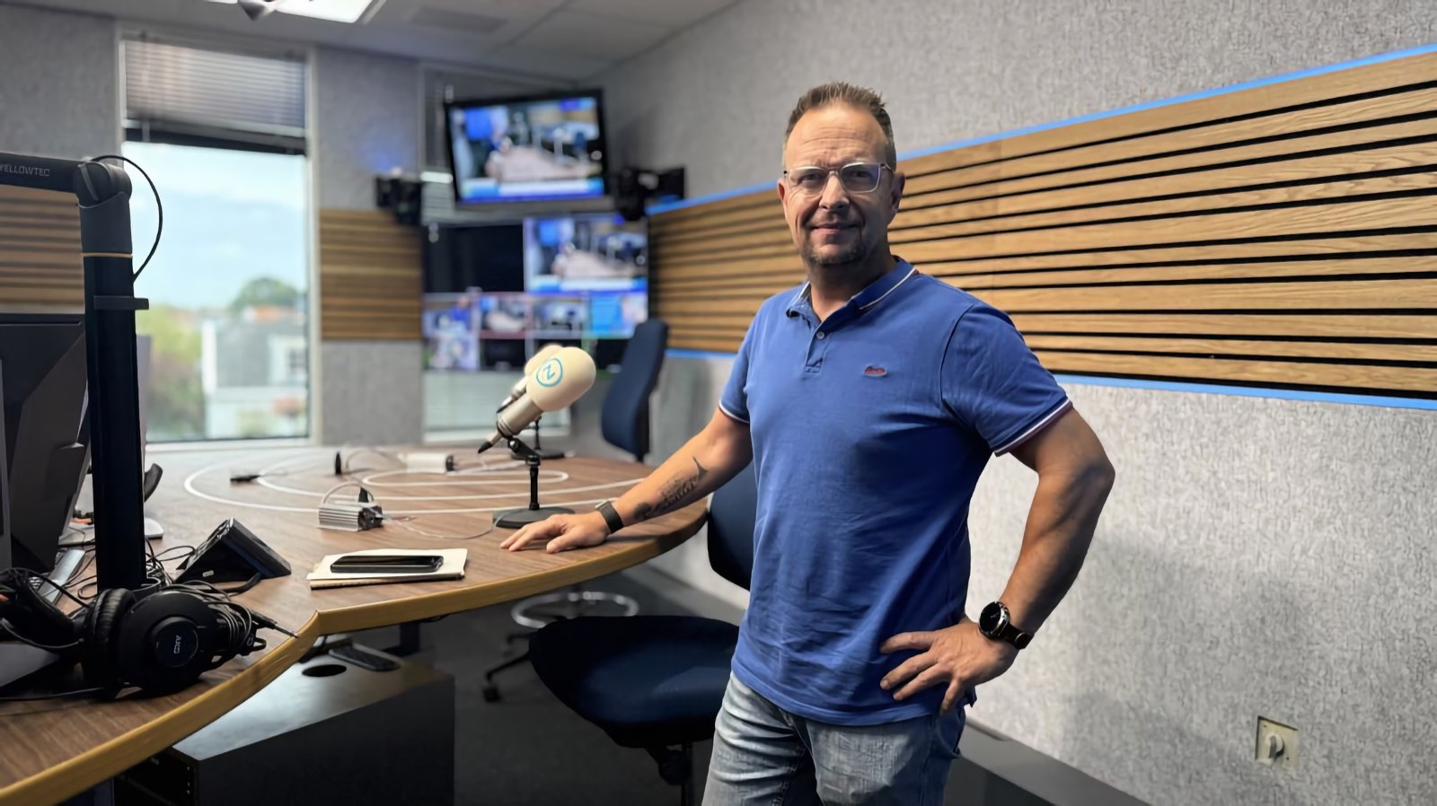 Theo van der Sluijs staat in de radiostudio van Omroep Zeeland, met een hand op de tafel naast de microfoon